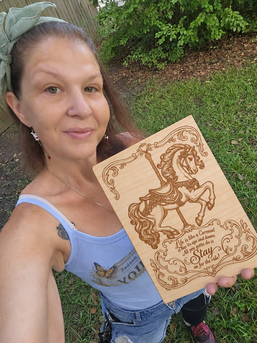 Lyddi holding a natural wood carousel horse sign outdoors