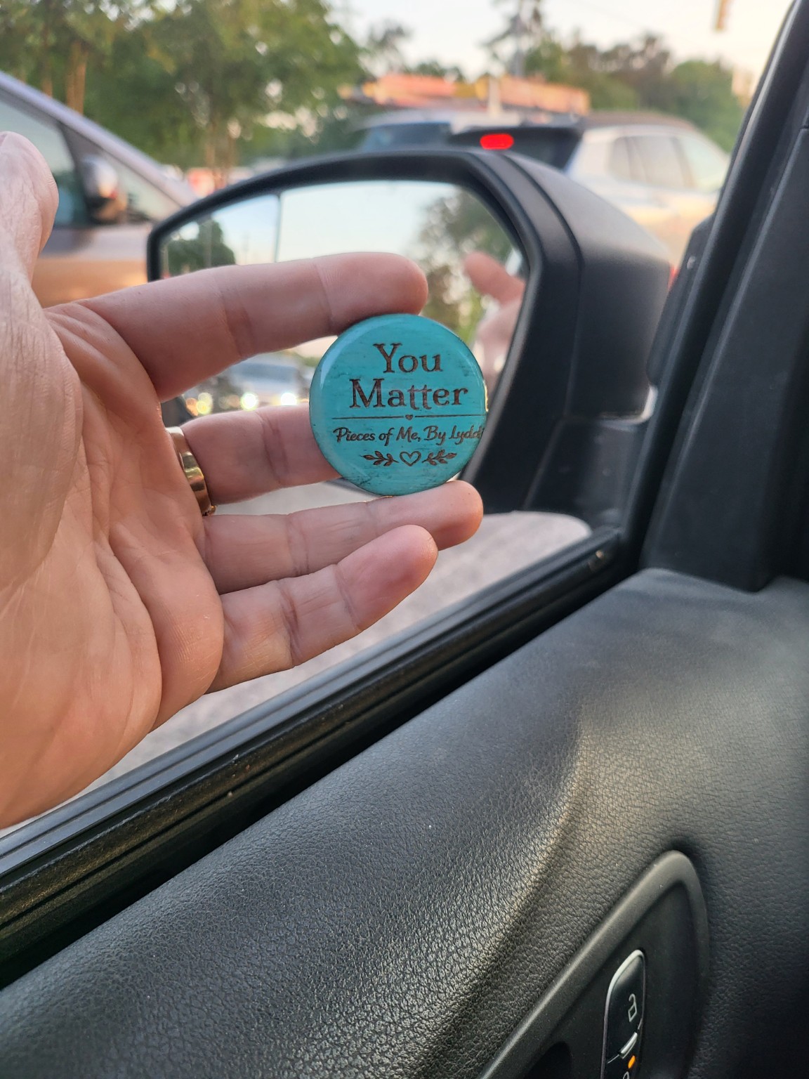 A turquoise You Matter token held near an open car window