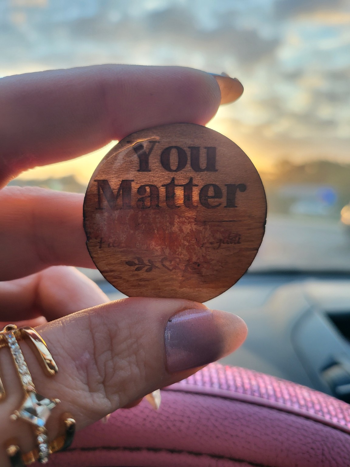 A You Matter token held toward a glowing sunset